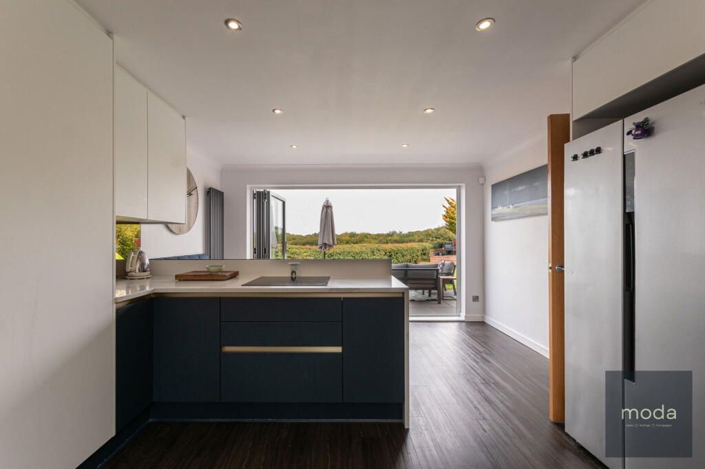 Modern kitchen with dark blue island, white cabinets, and view of outdoor seating.