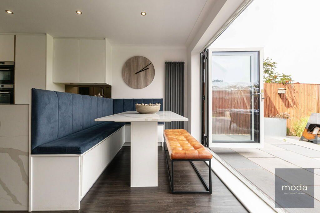 Modern kitchen with blue upholstered banquette, white table, and open glass doors to a patio.