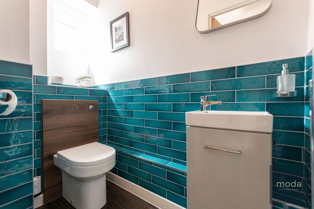 Small turquoise-tiled bathroom with a toilet, sink, and mirror.