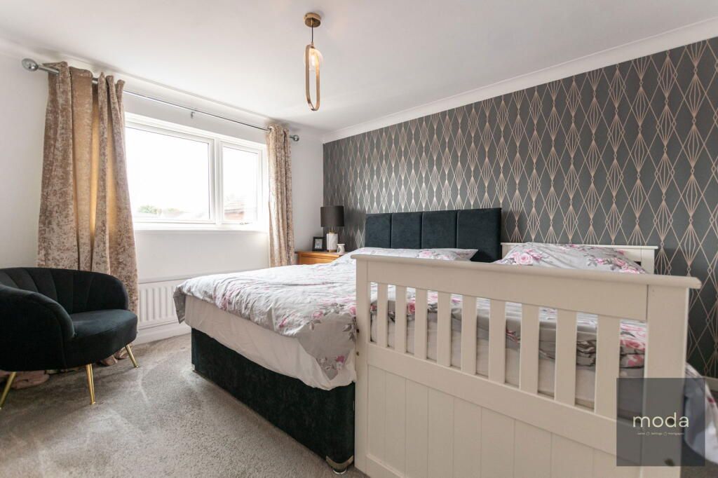 Bedroom with bed, armchair, window, patterned wallpaper, and a hanging light fixture.