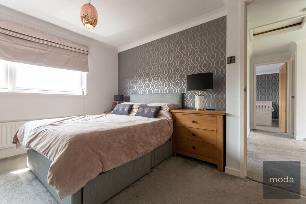Bedroom with bed, dresser, and patterned accent wall; neutral colors.