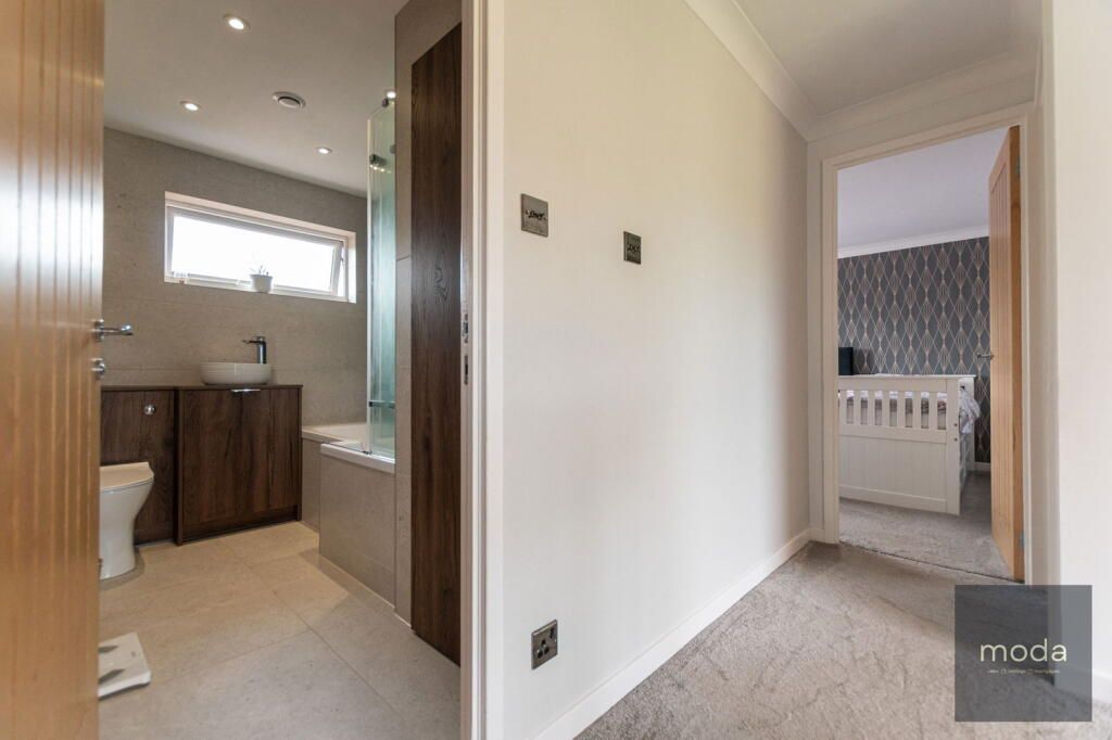 Hallway with doors to a bathroom and bedroom. Bathroom has a tub, sink, and toilet. Bedroom has a crib.
