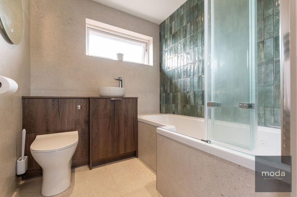 Modern bathroom with a toilet, cabinets, tub, and shower against green tiled wall.
