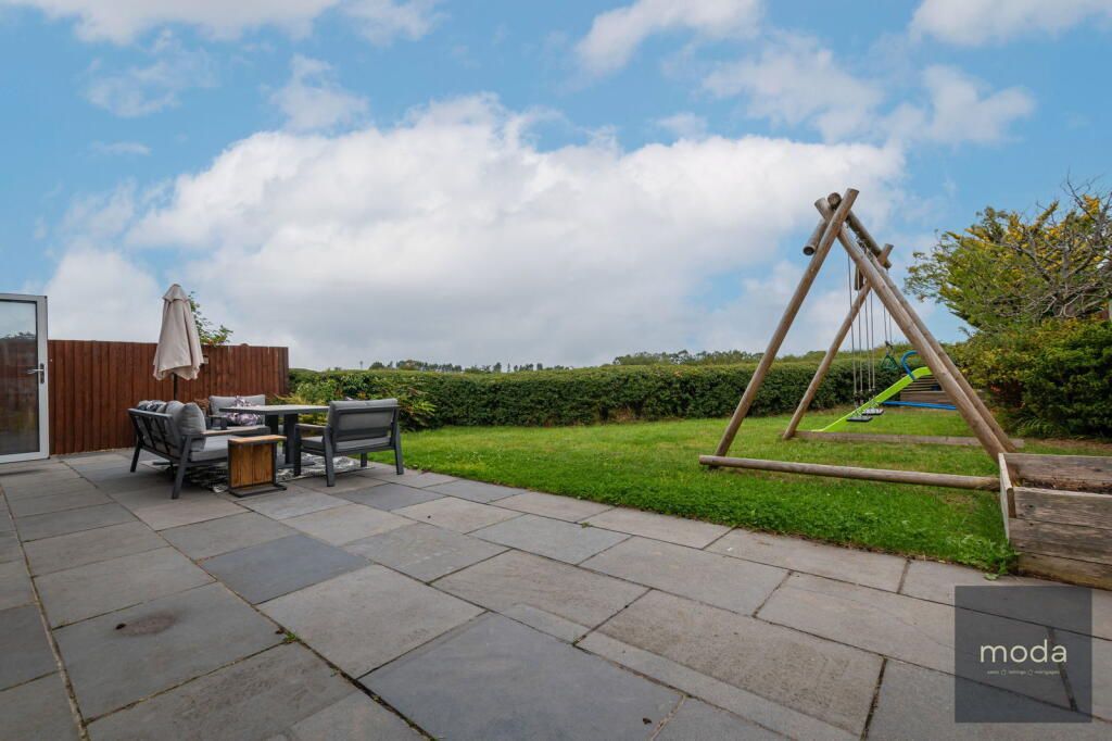 Patio with table, chairs, and swing set; green lawn, blue sky.