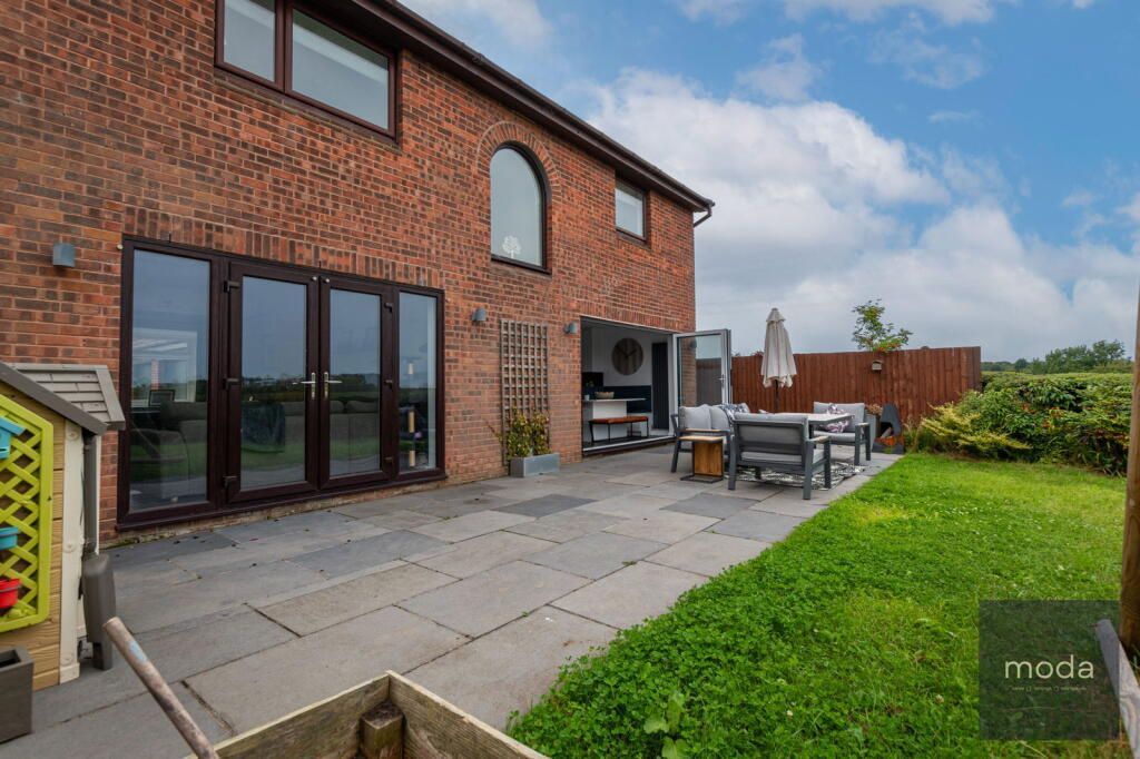 Backyard patio with gray pavers, brick house, lawn, and outdoor seating.