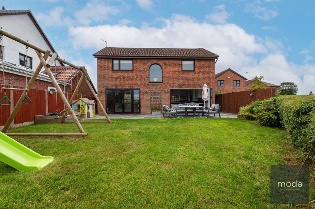 Backyard of a brick house with a large lawn, swing set, and outdoor seating.