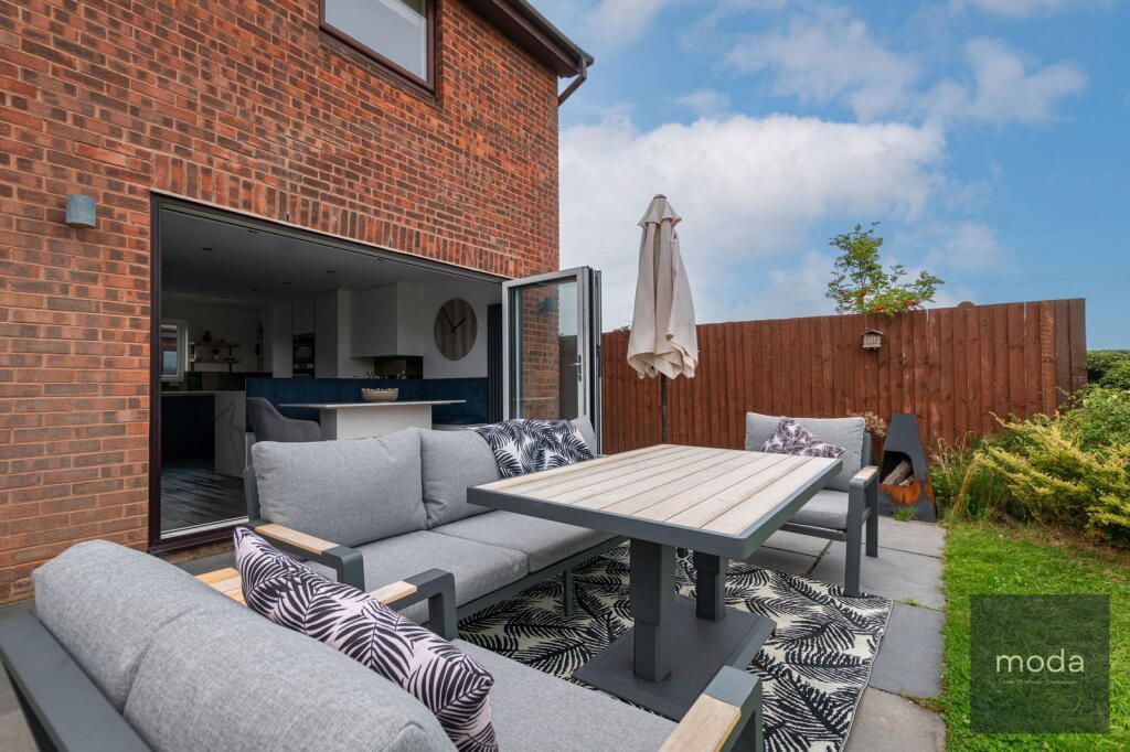 Patio with outdoor seating, open door to kitchen, brick exterior, sunny day.