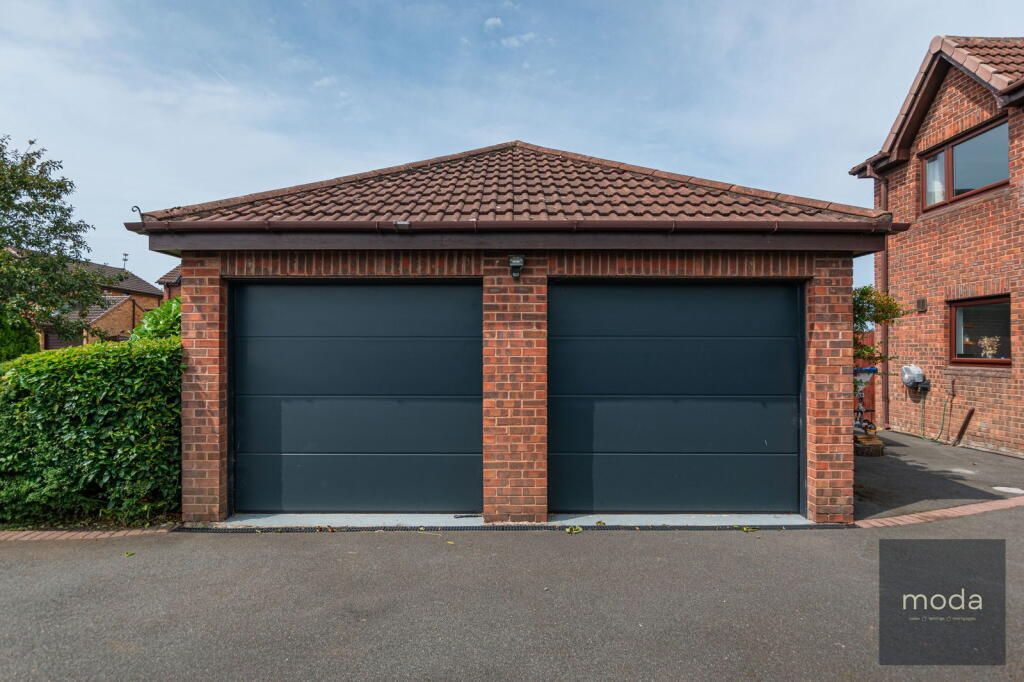Double garage with gray doors, brick walls, and a red tile roof, in front of a house on a sunny day.