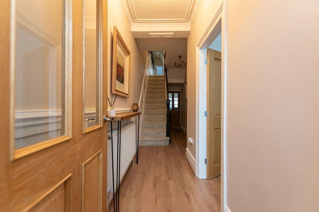 Hallway with wood flooring, stairs, console table, and light peach walls.