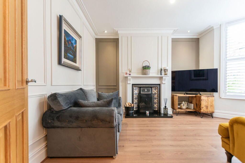 Living room with gray sofa, fireplace, wooden floor, and TV.