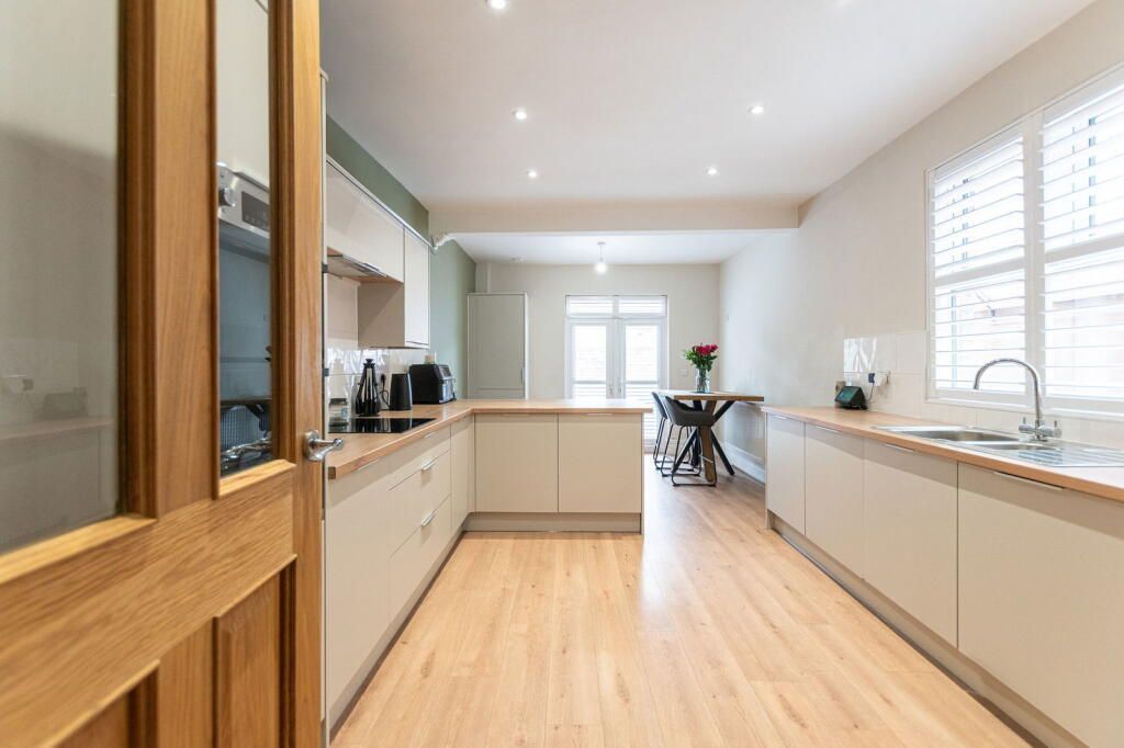 Bright, modern kitchen with light wood floors, countertops, and cream cabinets. A table and window are in the background.