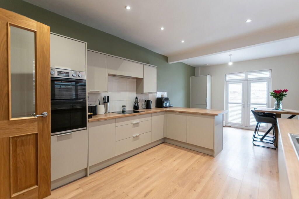 Modern kitchen with pale cabinets, wood countertops, wooden floor, and green wall.