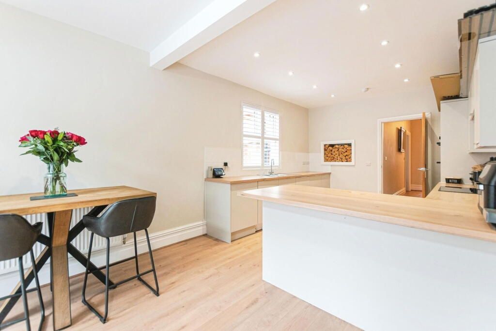 A modern kitchen with a wooden breakfast bar, dining table with flowers, and light wood flooring.