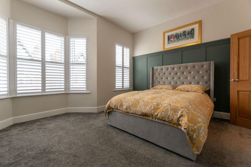 Bedroom with gray bed, yellow bedding, bay windows, and dark green accent wall.