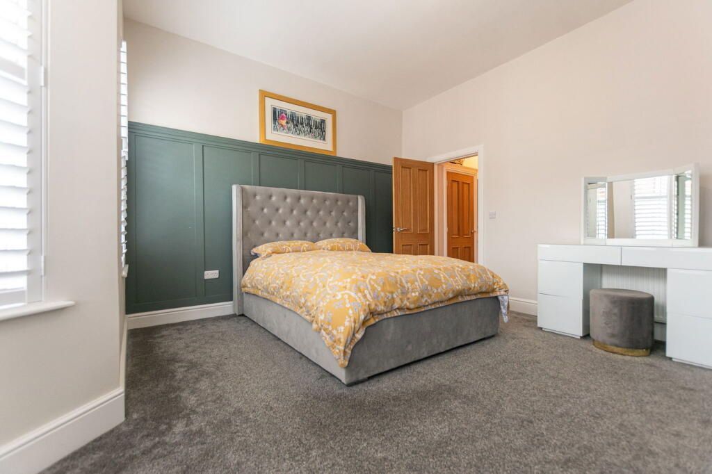 Bedroom with gray carpet, bed, green panel wall, white vanity, and gold bedding.