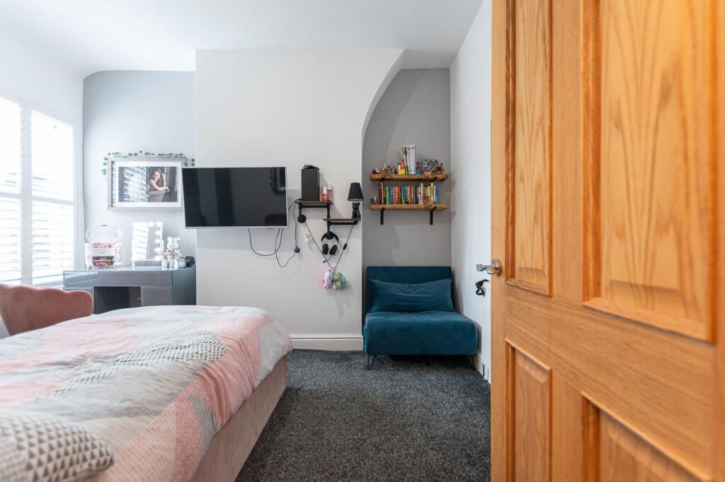 Bedroom with a bed, TV, blue chair, and arched shelf; ajar wooden door on the right.