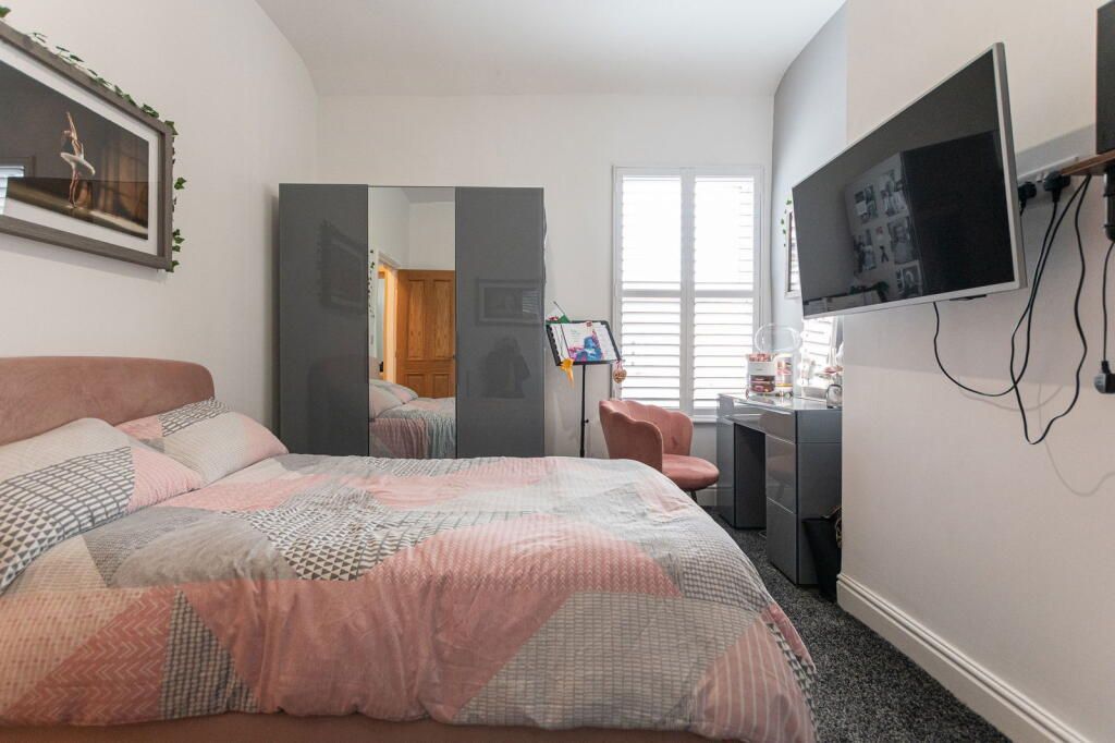 Bedroom with pink bedding, gray wardrobe and desk, TV on the wall.