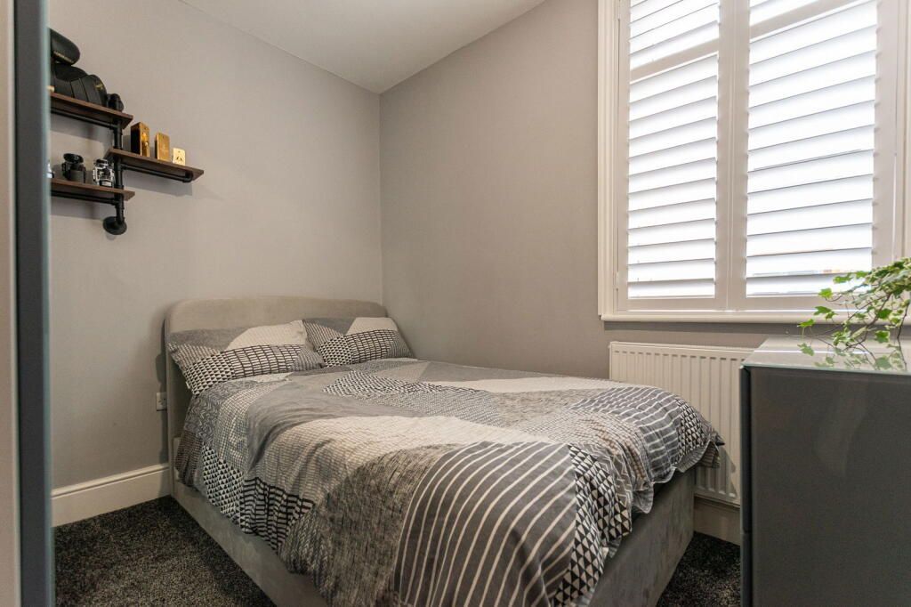 Small bedroom with gray walls, a bed, window with shutters, and a shelf with decor.