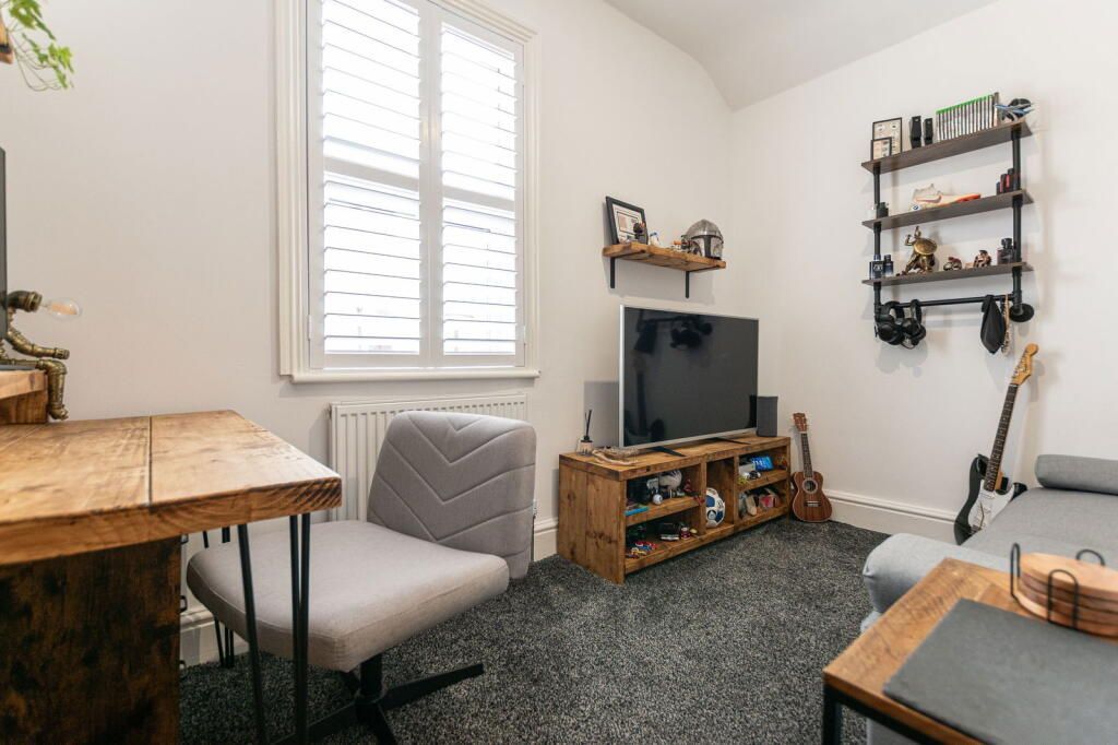 Cozy room with desk, chair, TV, guitar, and shelves, showcasing a modern, minimalist style.