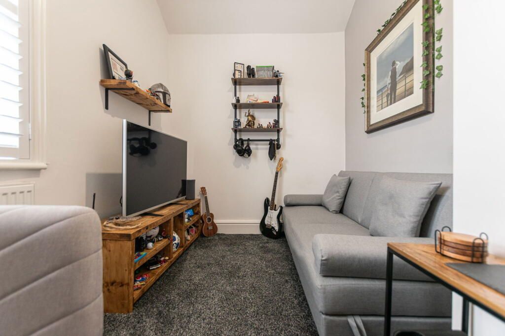 Cozy living room with gray sofa, wooden shelves, TV, and guitar.