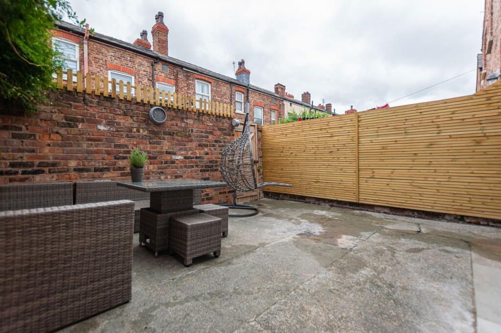 Patio with brown wicker furniture, brick wall, and wooden fence under overcast sky.