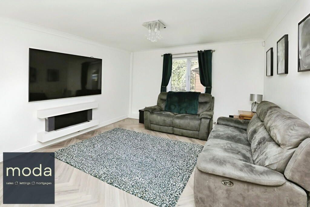 Spacious living room with gray couches, large TV, green rug, and window with green curtains.