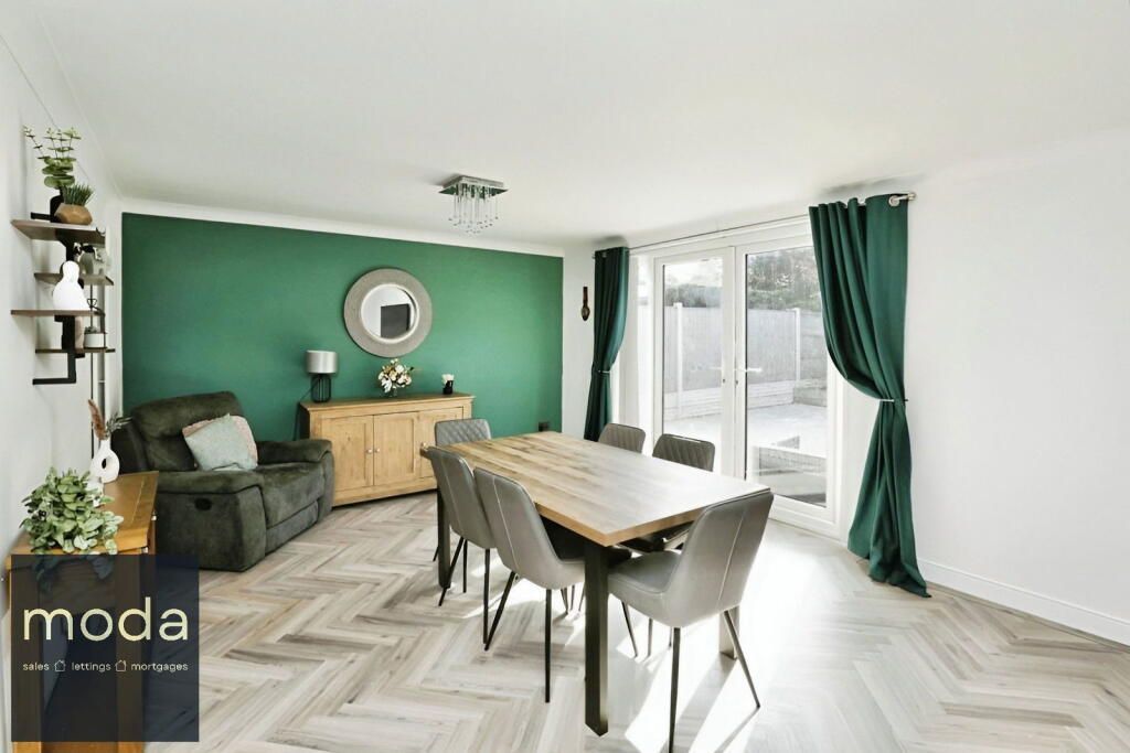 Dining area with wooden table and chairs, green accent wall, and outdoor view.