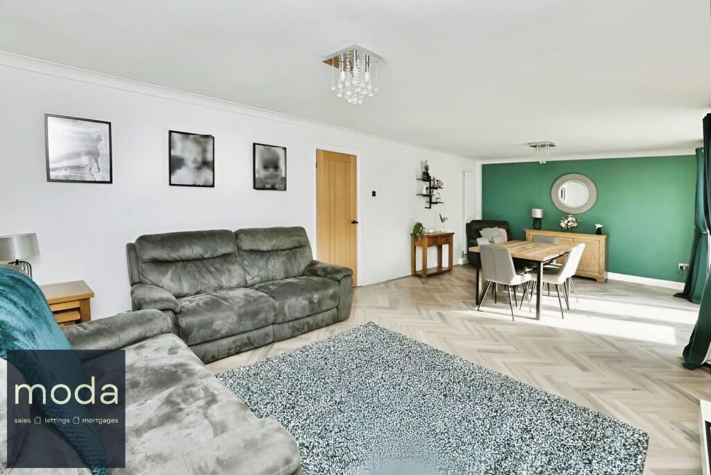Spacious living room with gray sofa, dining area with green accent wall, herringbone floors.