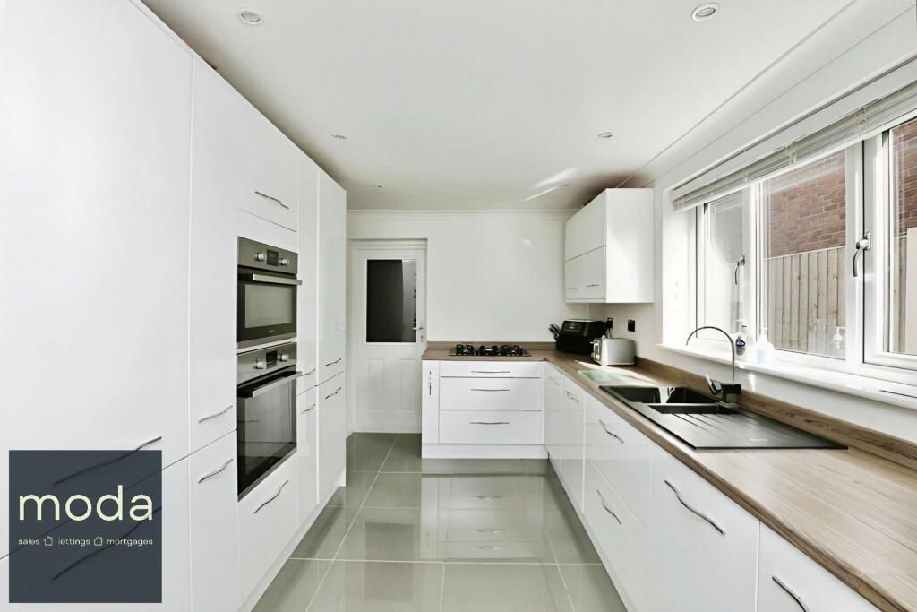 Modern white kitchen with light wood countertop and stainless steel appliances.