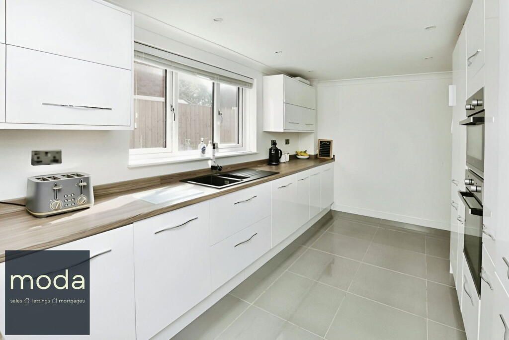 Modern white kitchen with cabinets, oven, and gray tile floor.