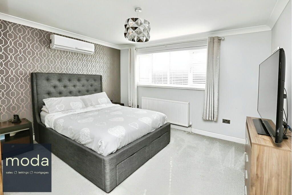 Bedroom with gray bed, patterned wallpaper, large TV, and window with curtains.