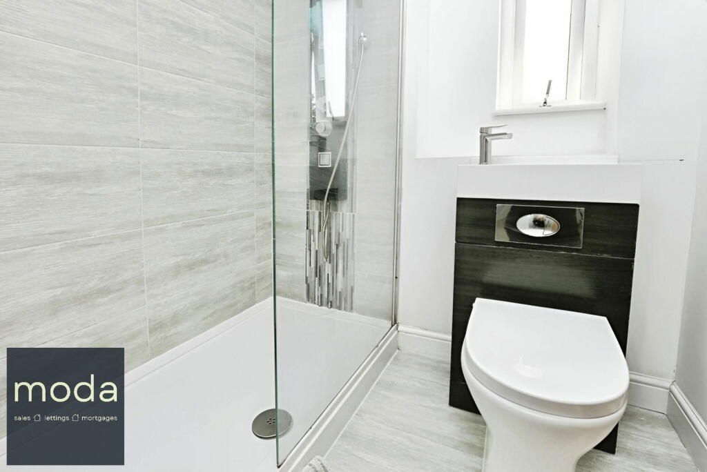 Small, modern bathroom with a shower stall and toilet. White and gray tiles and black cabinet.