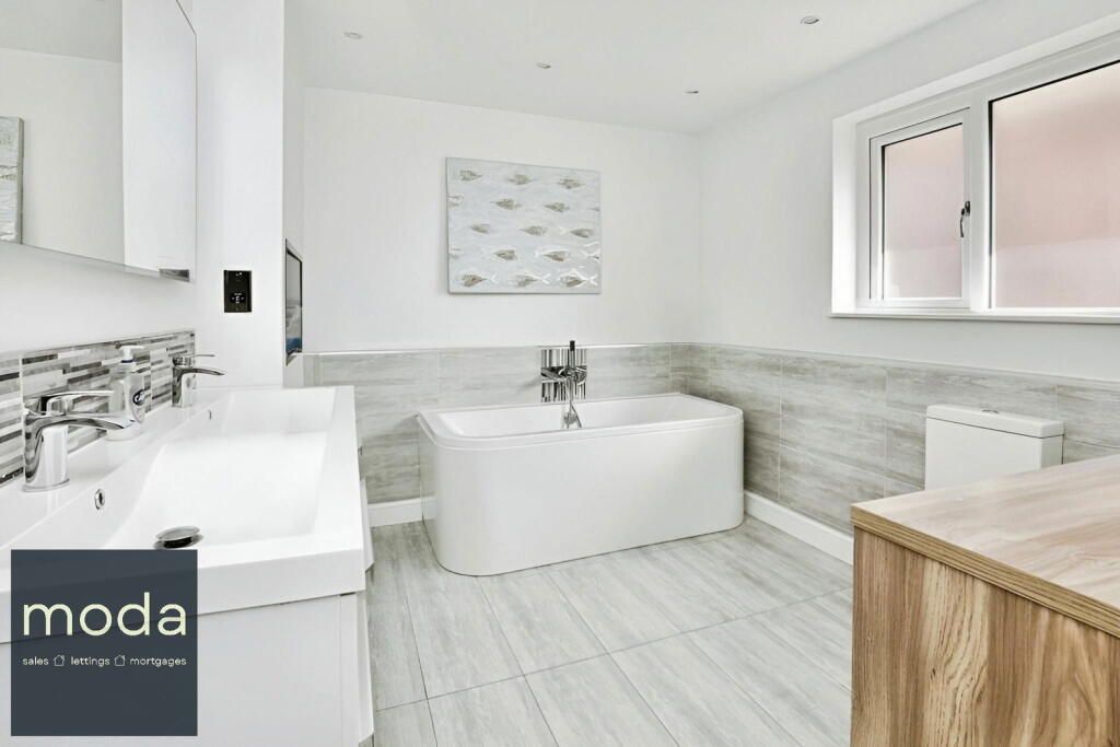 Modern white bathroom with a freestanding tub, vanity, and natural light.