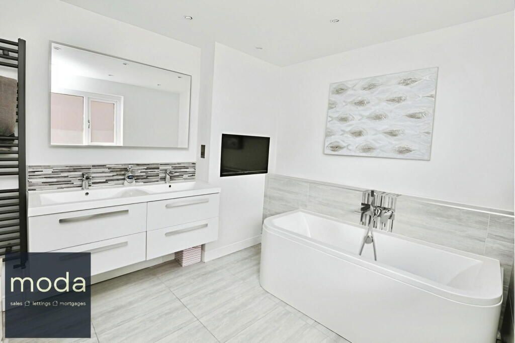 Modern white bathroom with a bathtub, double sink vanity, and mounted TV.