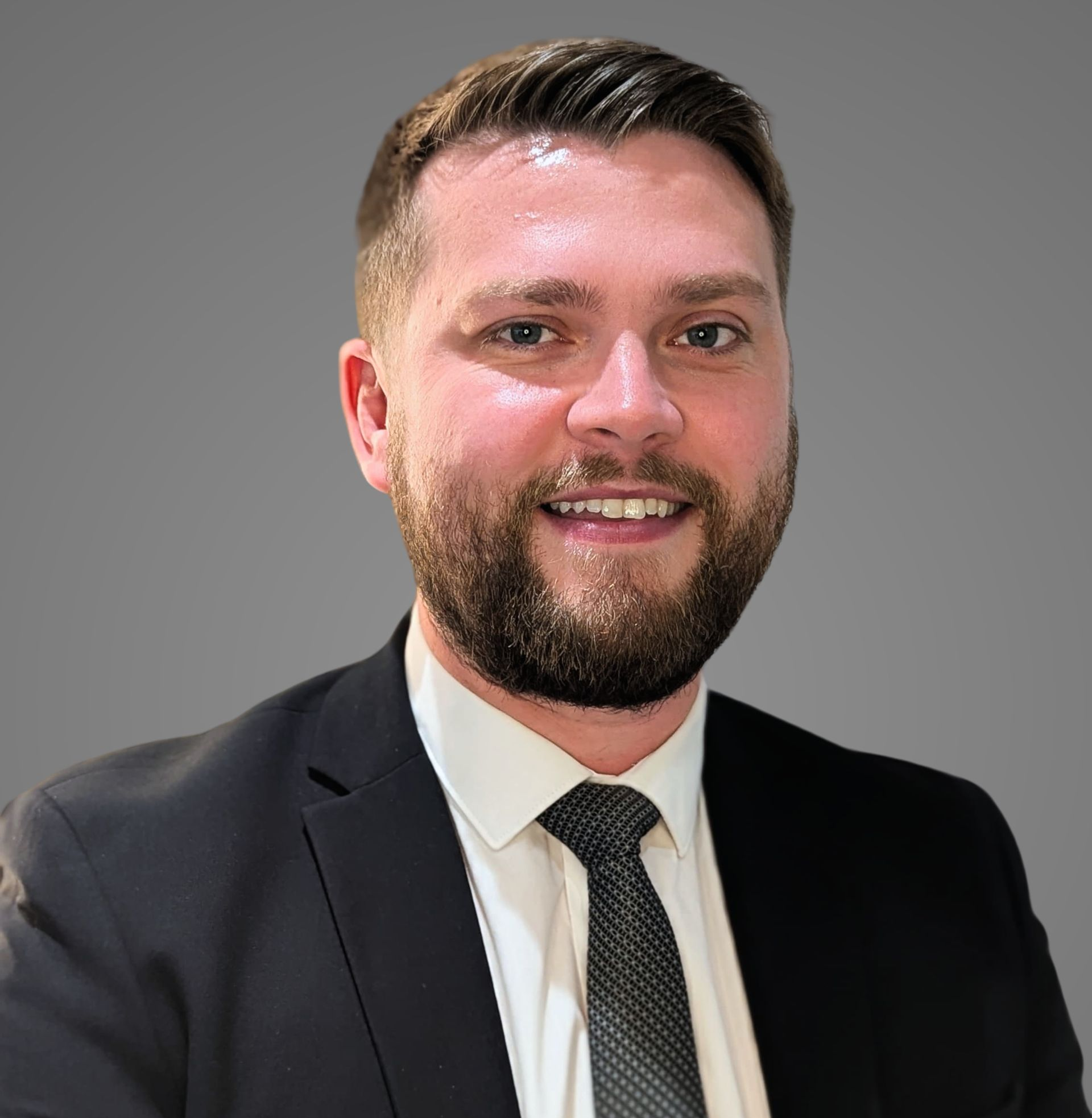 Man in a suit smiles at the camera against a gray background.