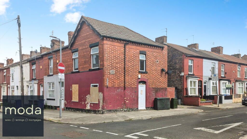 A red brick corner building with boarded-up windows, next to terraced houses, on a street.