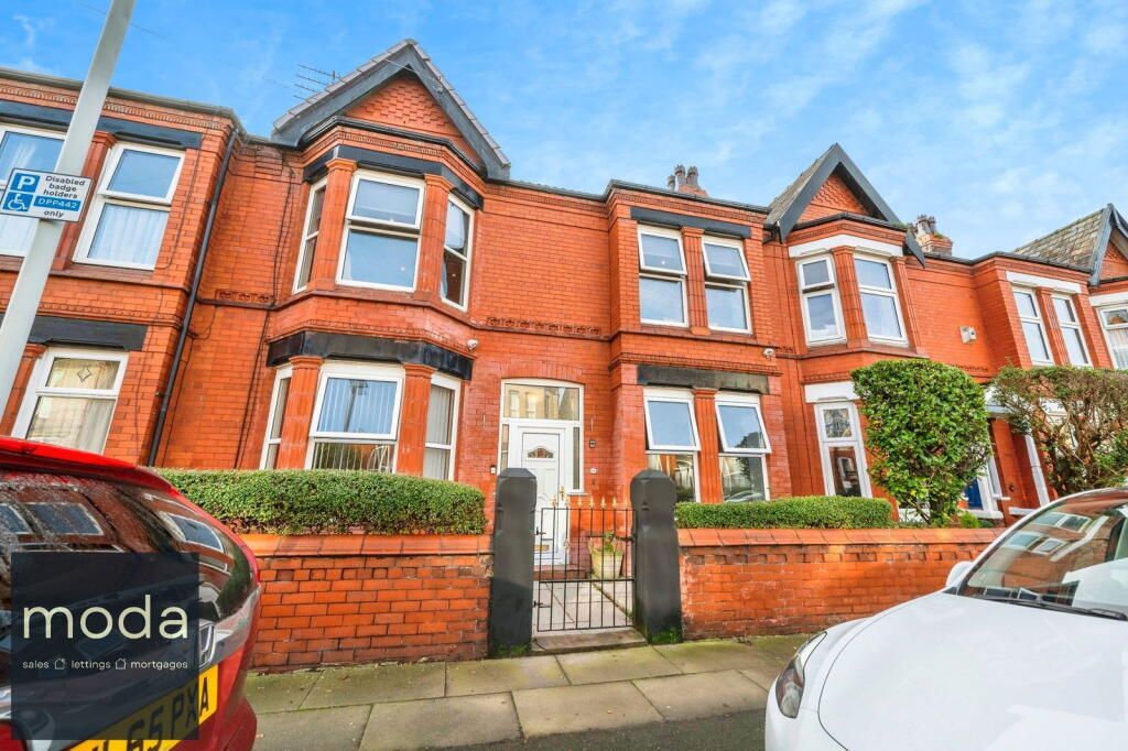 Red brick terraced houses with white windows and a small garden, parked cars on the street.