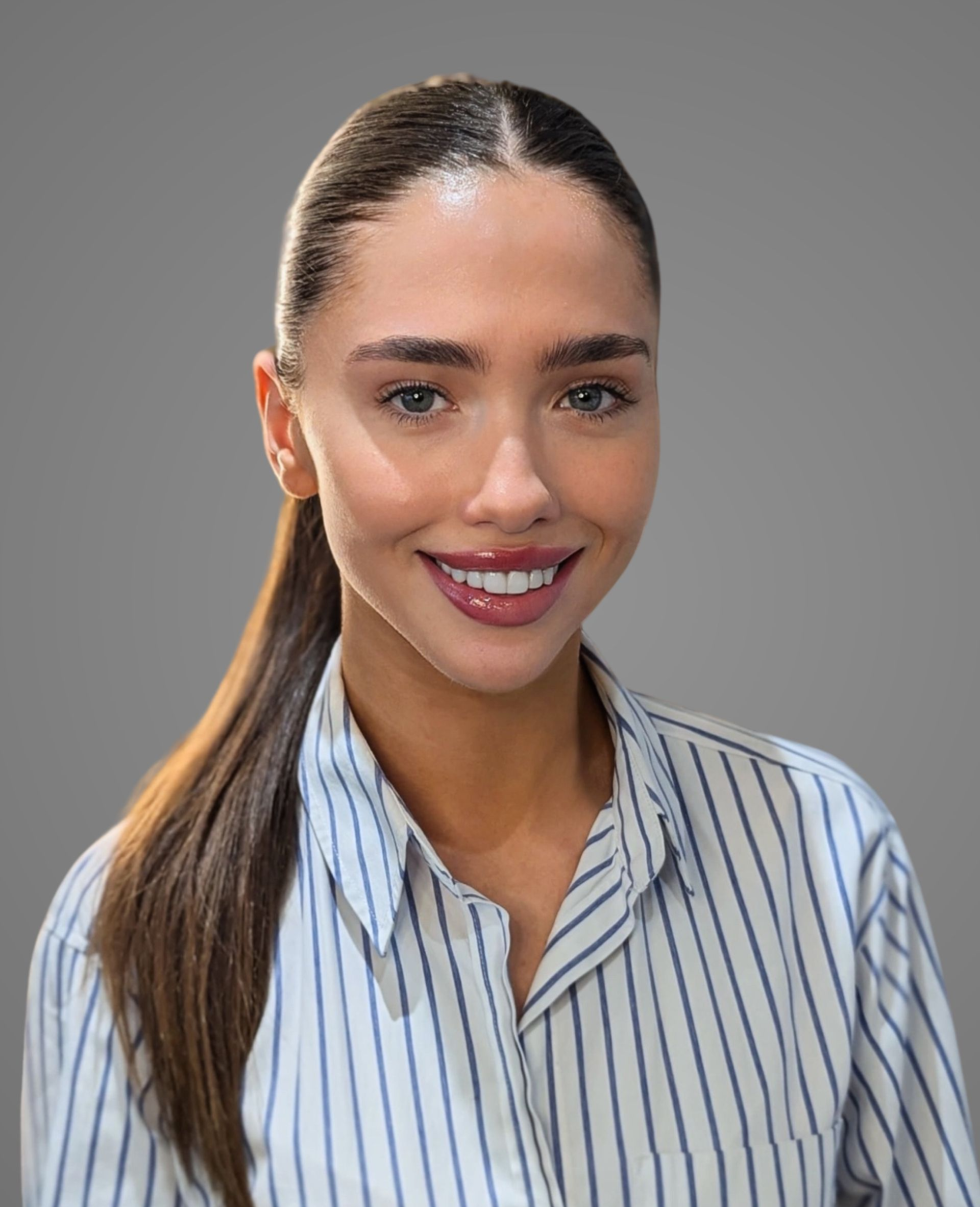 Woman with brown hair in a ponytail, smiling, wearing a striped shirt against a gray background.