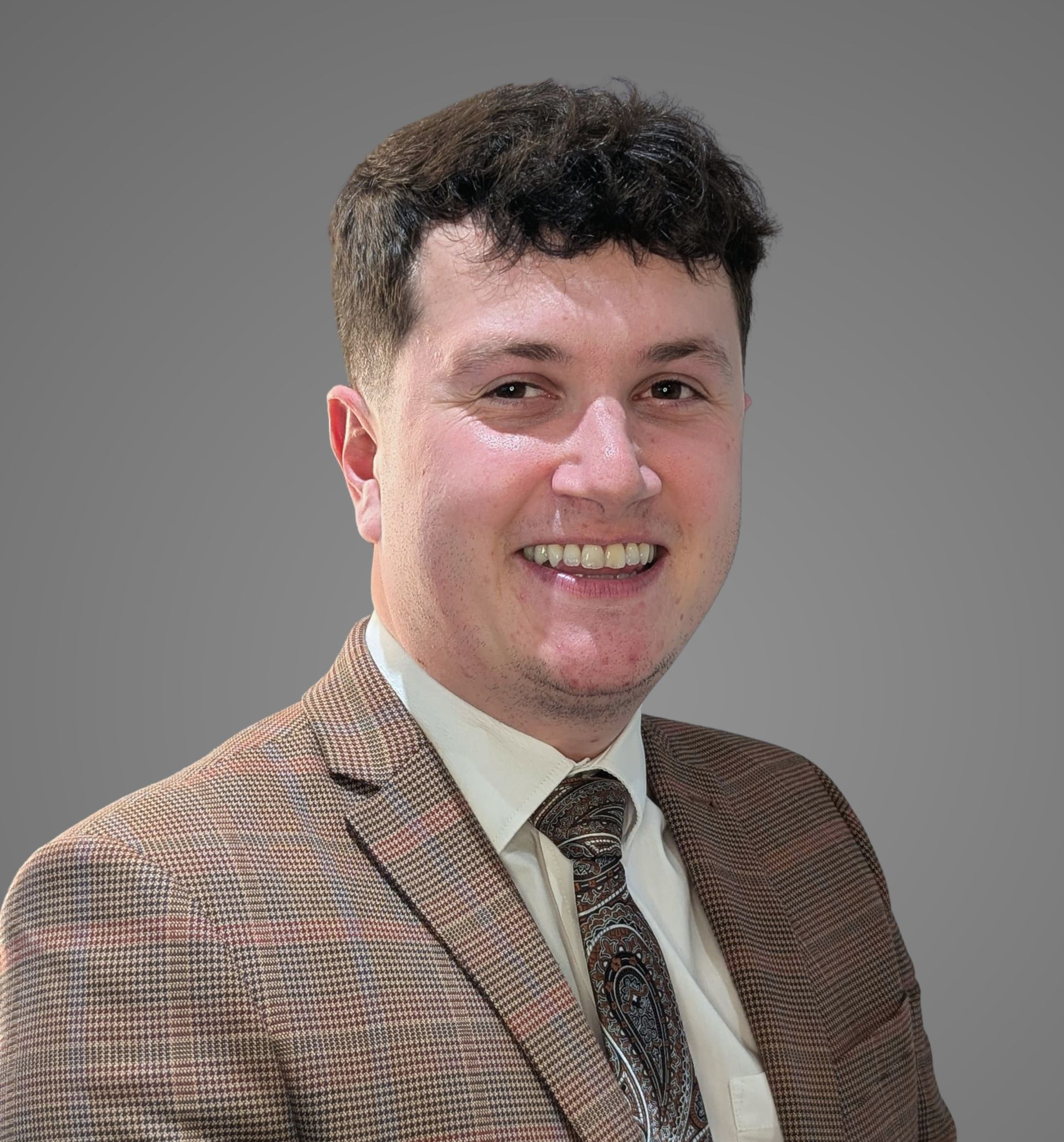 Man in a brown patterned suit smiling, looking at the viewer.