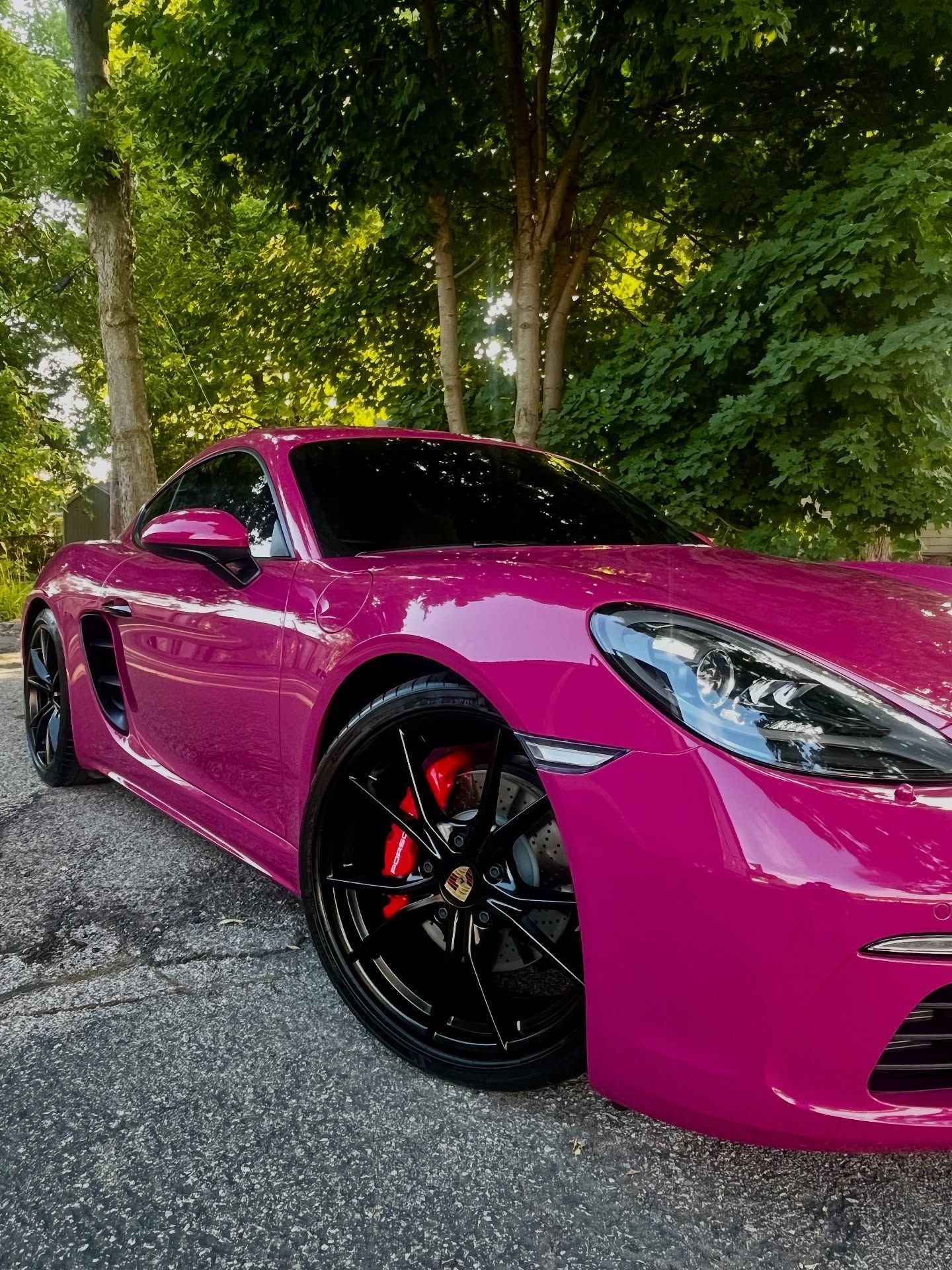Magenta Porsche sports car with black wheels and red brake calipers parked on asphalt.