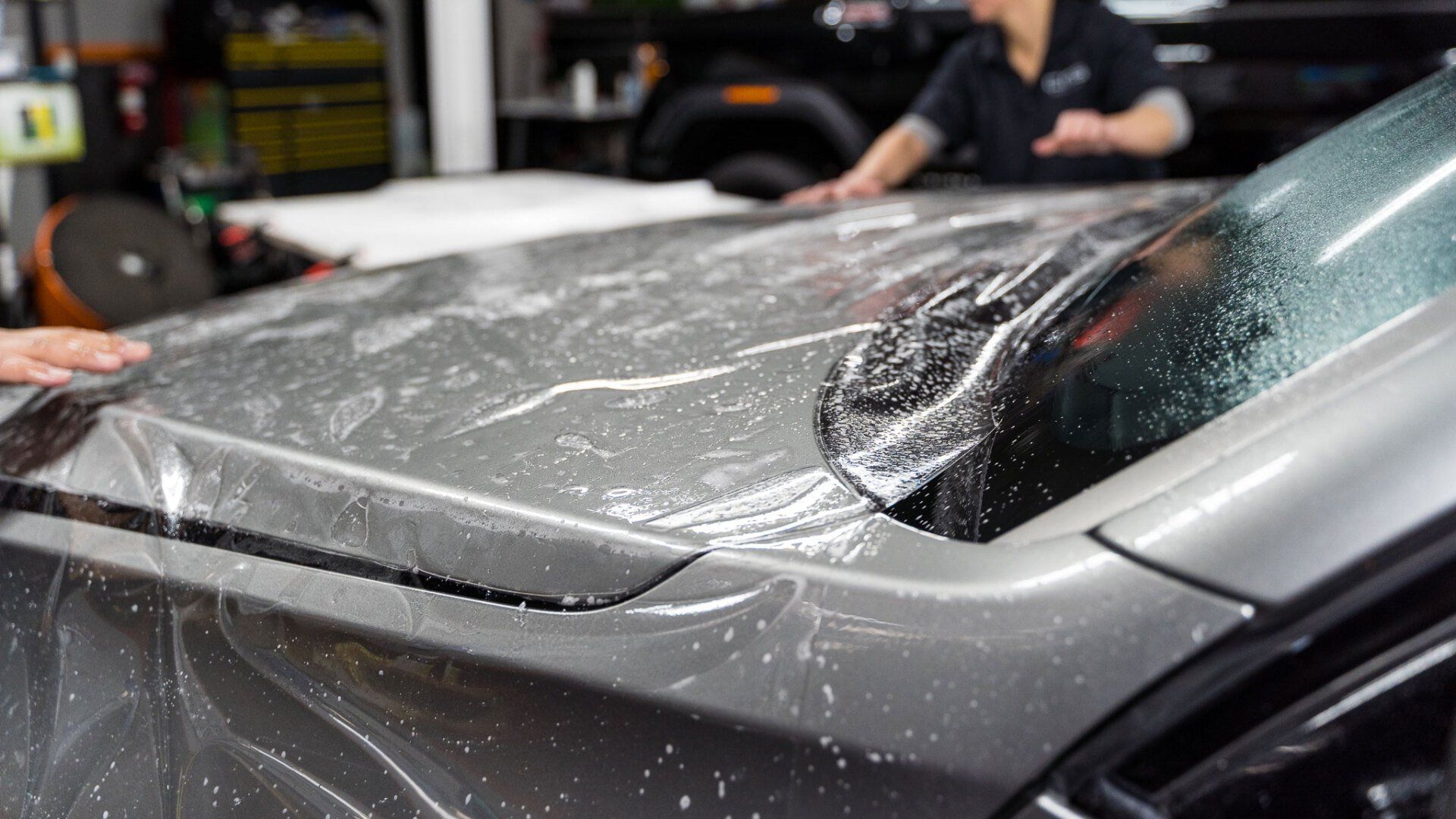 Car hood being covered with clear protective film by two people in a garage.
