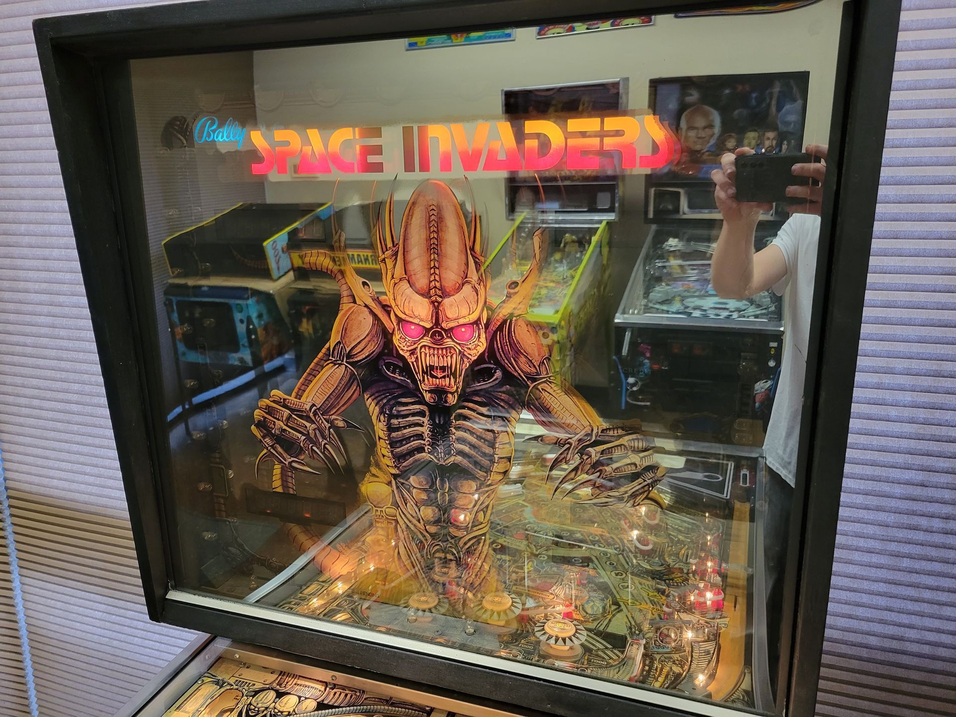 A man is taking a picture of a space invaders pinball machine