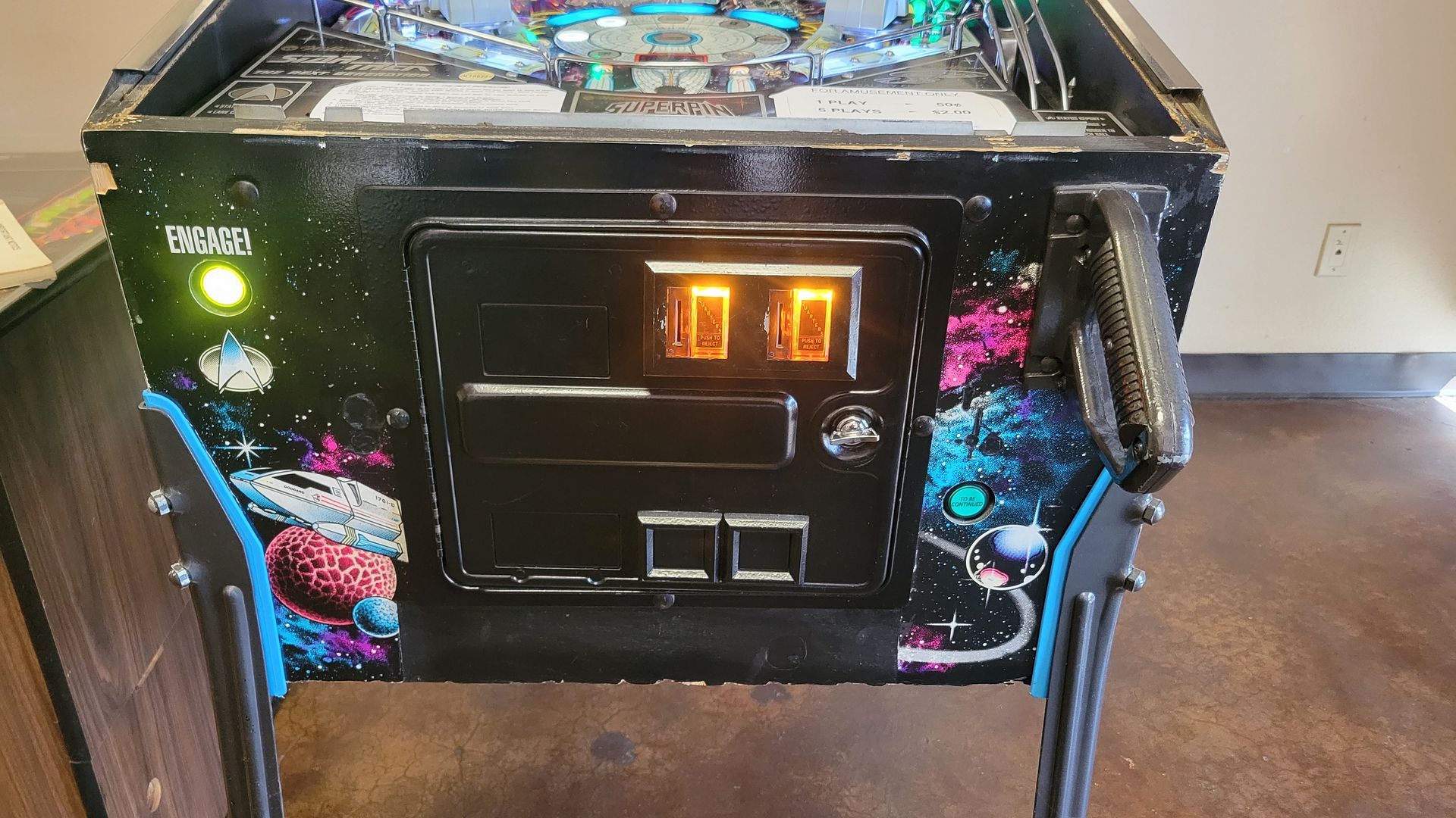 A pinball machine is sitting on a concrete floor in a room.