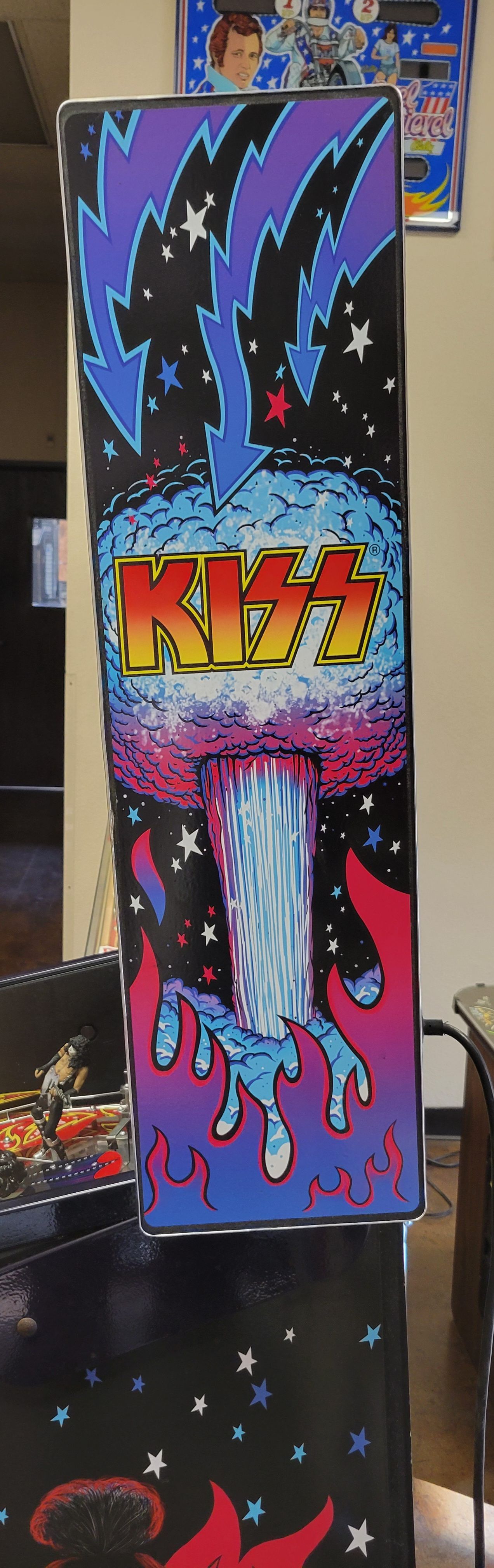 A kiss arcade machine is sitting on a table in a living room.