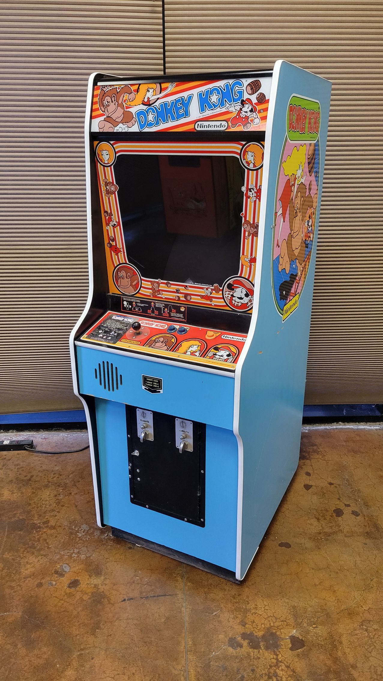 A blue arcade game is sitting on a concrete floor.