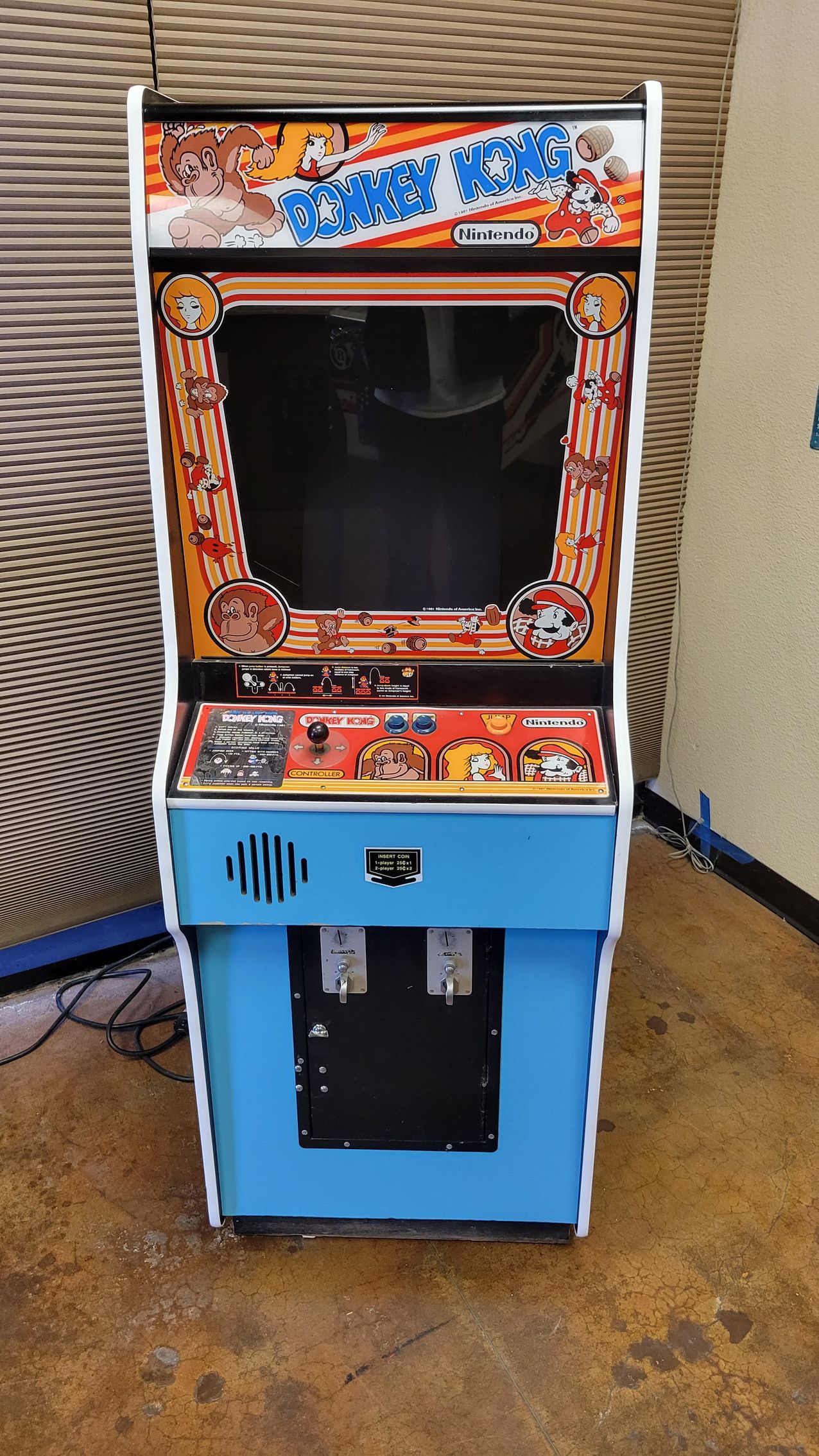 A blue and white arcade game is sitting on a wooden floor.