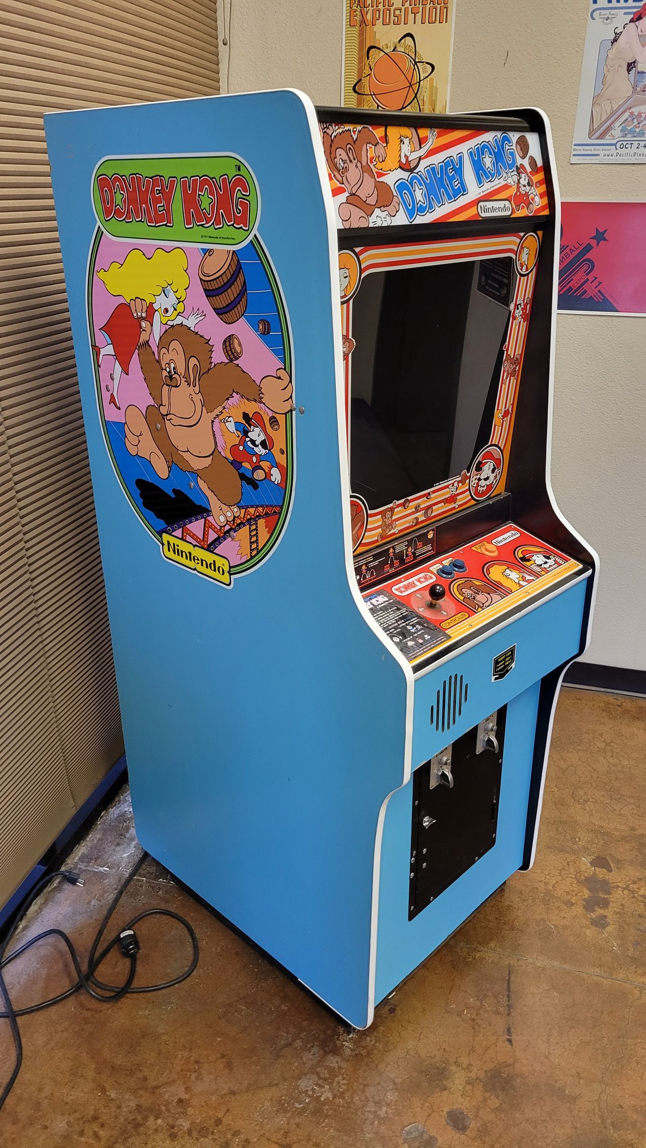 A blue arcade game is sitting on the floor in a room.