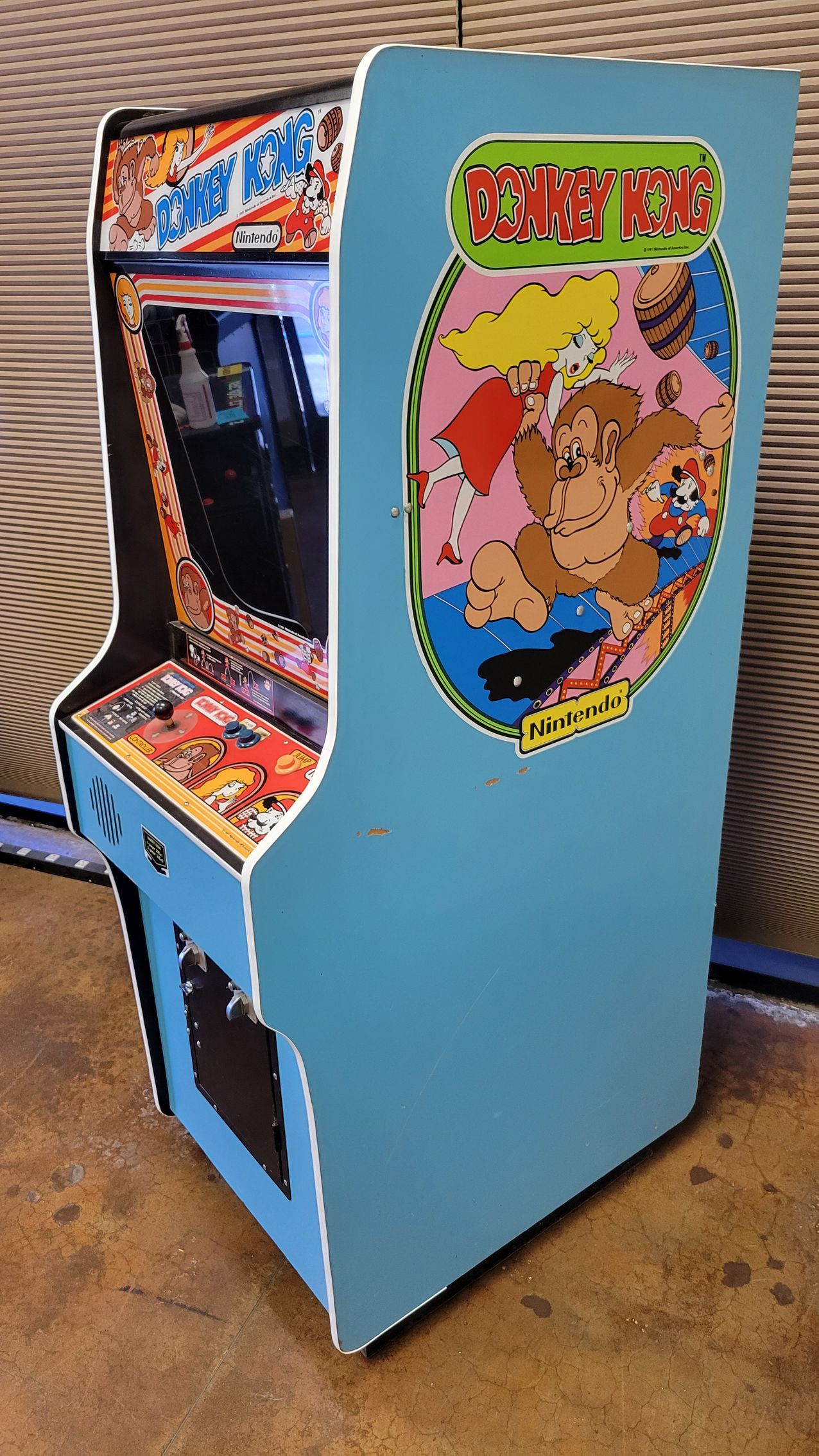 A donkey kong arcade game is sitting on a wooden floor.