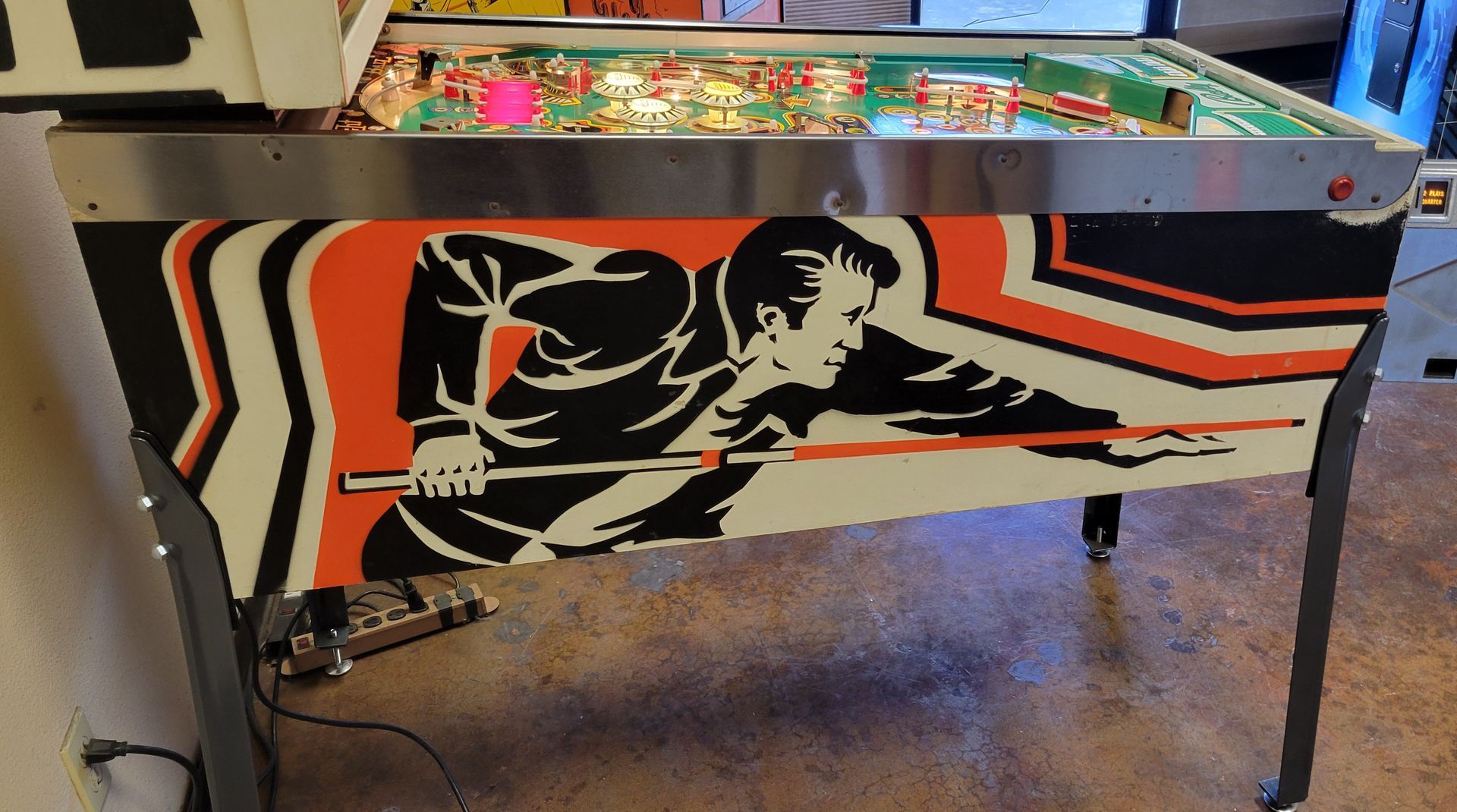 A pinball machine with a man playing pool on it