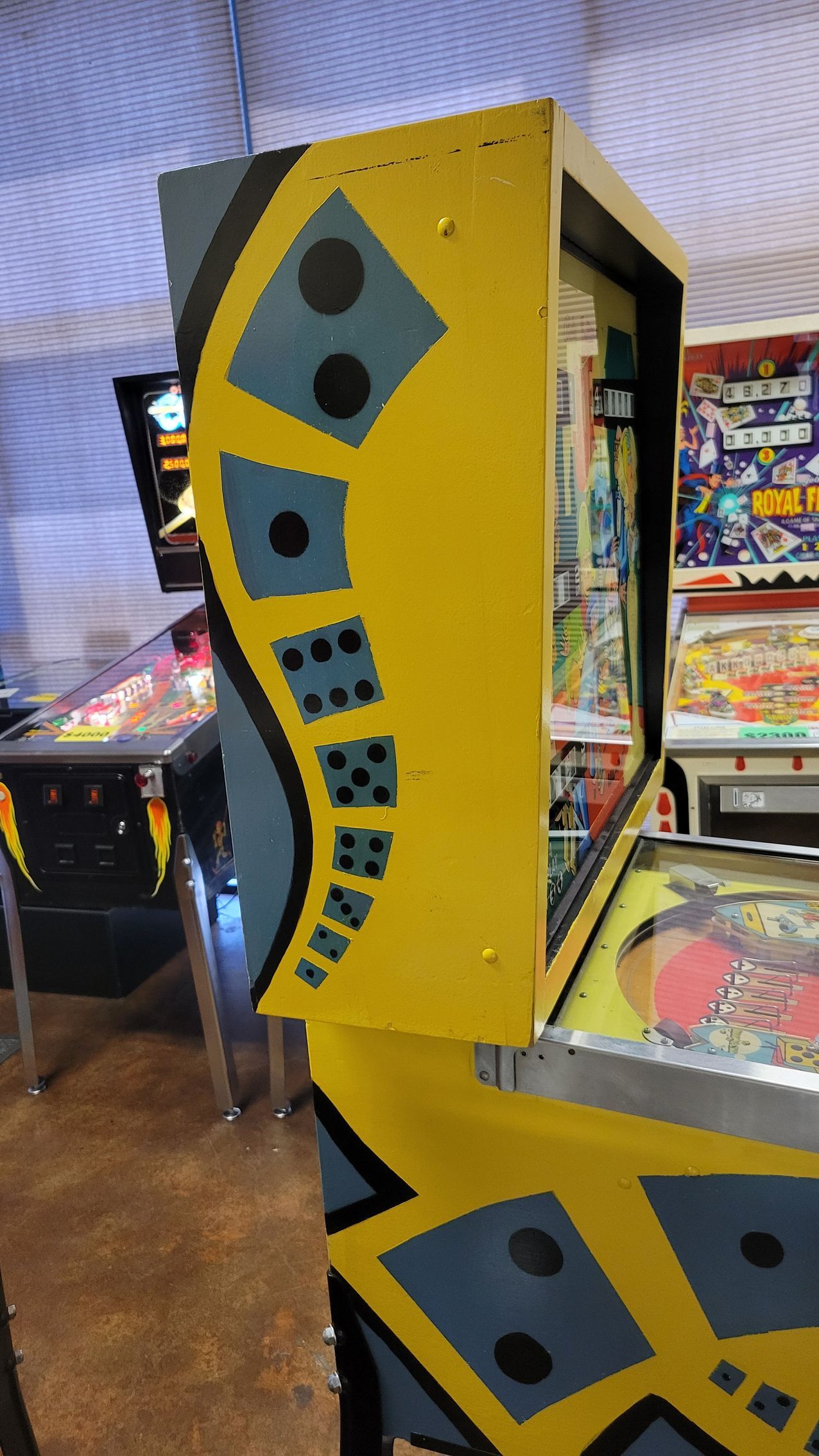 A yellow pinball machine is sitting in a room with other pinball machines.